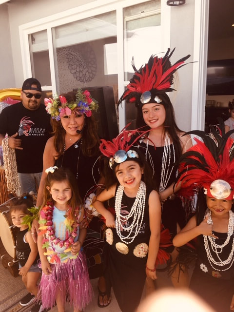 Families in Hawaiian party costumes with leis and feathered headpieces