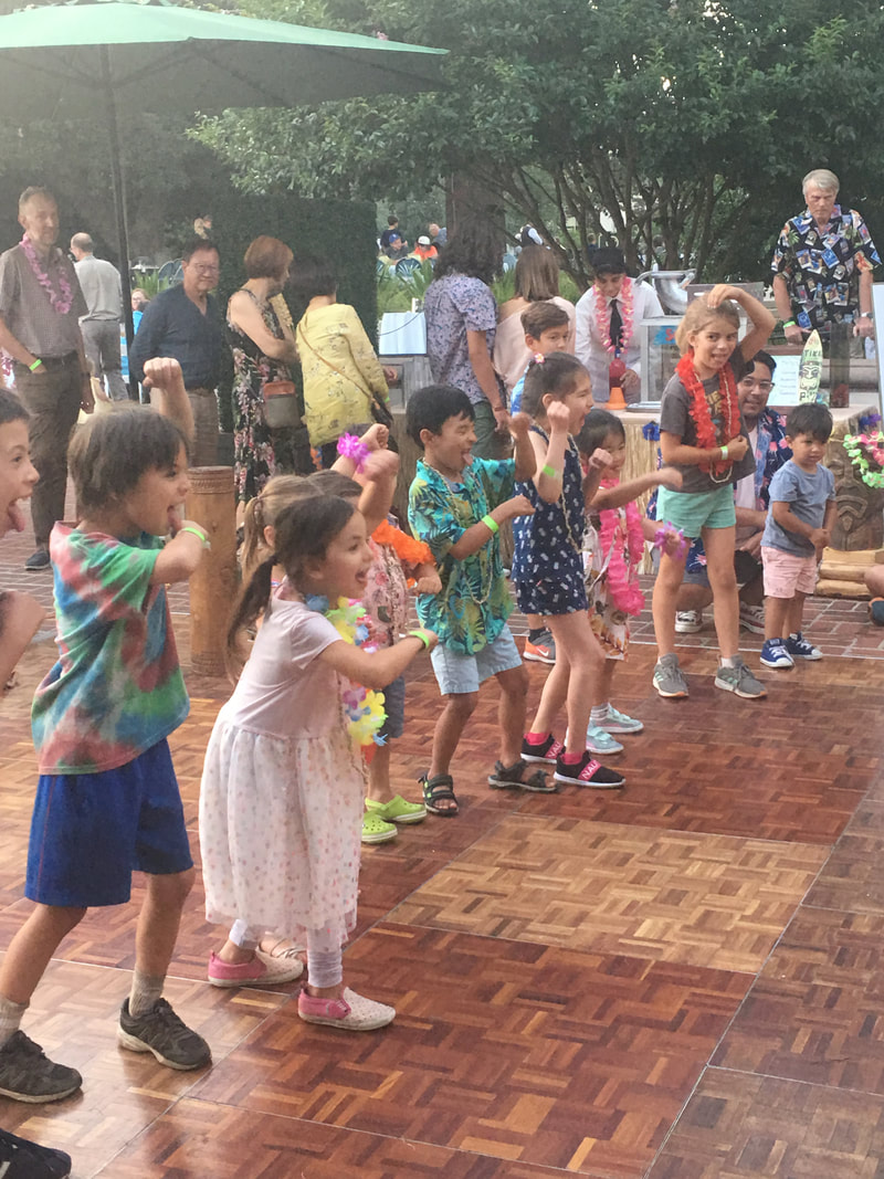 Children wearing colorful leis dancing at an outdoor luau community event